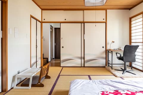 A Japanese-style bedroom with tatami mat floors, fusuma sliding doors, and a desk with an office chair in the corner.