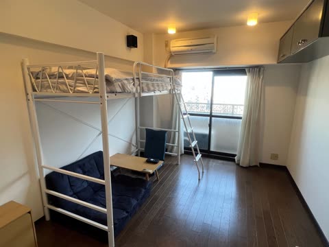 A white loft bed is positioned over a blue futon and small table in a room with dark wood floors and a sliding glass door.