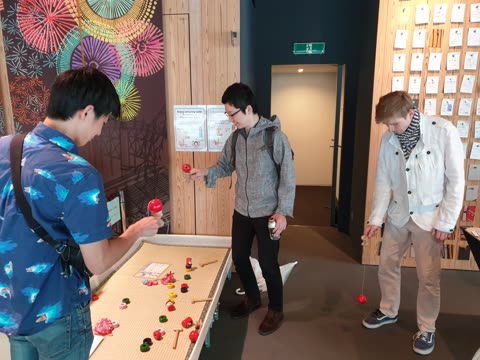 Three people playing kendama and other traditional Japanese toys indoors.