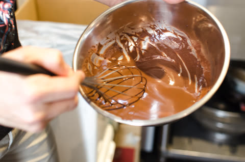 Person whisking brown liquid in metal bowl.