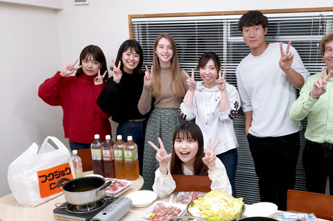 A group of seven people make peace signs while posing for a photo around a table with hot pot ingredients.