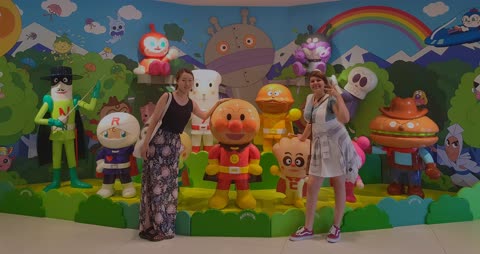Two women pose with large cartoon character statues inside.