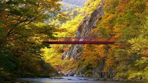 Red suspension bridge spanning a river gorge amid autumn foliage.