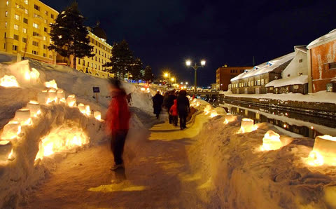People walking along a snow-lined canal at night, illuminated by snow lanterns.