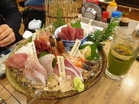 Person eating sashimi and drinking green beer at a restaurant.