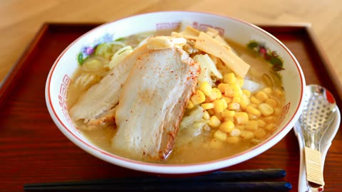 Bowl of ramen with pork, corn, and bamboo shoots on a wooden tray.