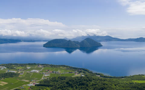 Aerial view of island in lake, surrounded by green land and clouds.