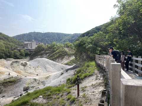 Four people stand on a wooden boardwalk overlooking a hilly, light-grey landscape.