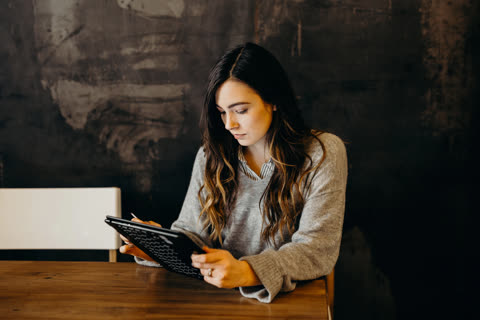 Woman uses stylus on tablet at a wooden table.