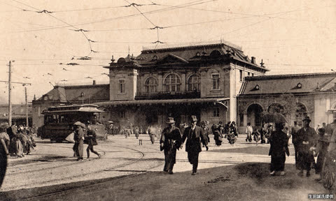 Two men walking near a train station and streetcar.