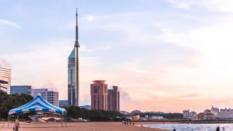 Tall tower and buildings on a sandy beach at sunset.