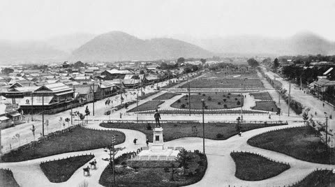 Black and white aerial view of a city park with a statue, roads, and buildings.