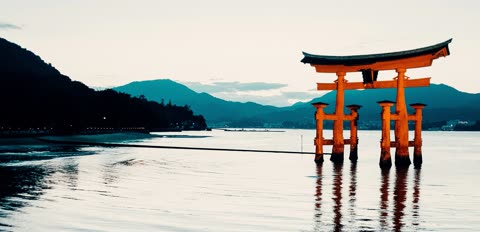 Orange torii gate stands in calm water, mountains in background.