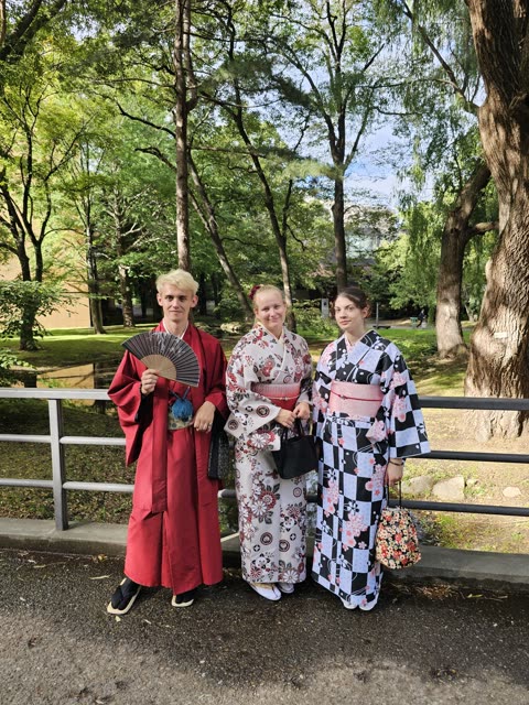 Three people in kimonos stand by a park fence.