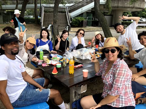 Group of people picnicing at a park table, making peace signs.