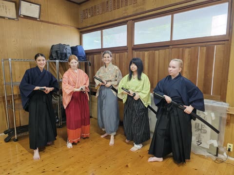 Four women holding swords in a wooden-floored dojo.