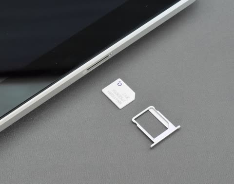 SIM card and tray on gray surface near tablet.
