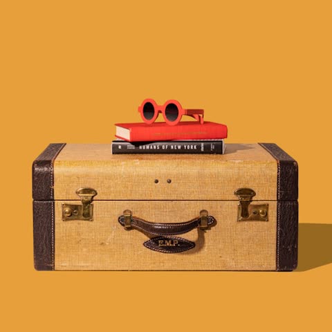 Red sunglasses rest on books atop a vintage suitcase.